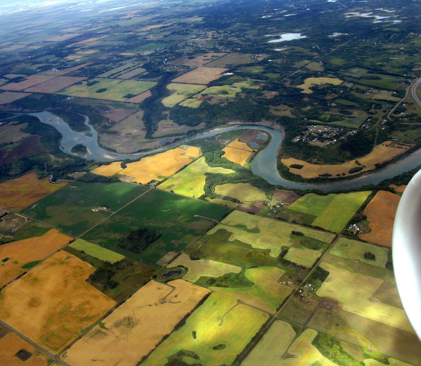 Aerial view of a river winding through aspen bluffs, cropland and small wetlands in late summer
