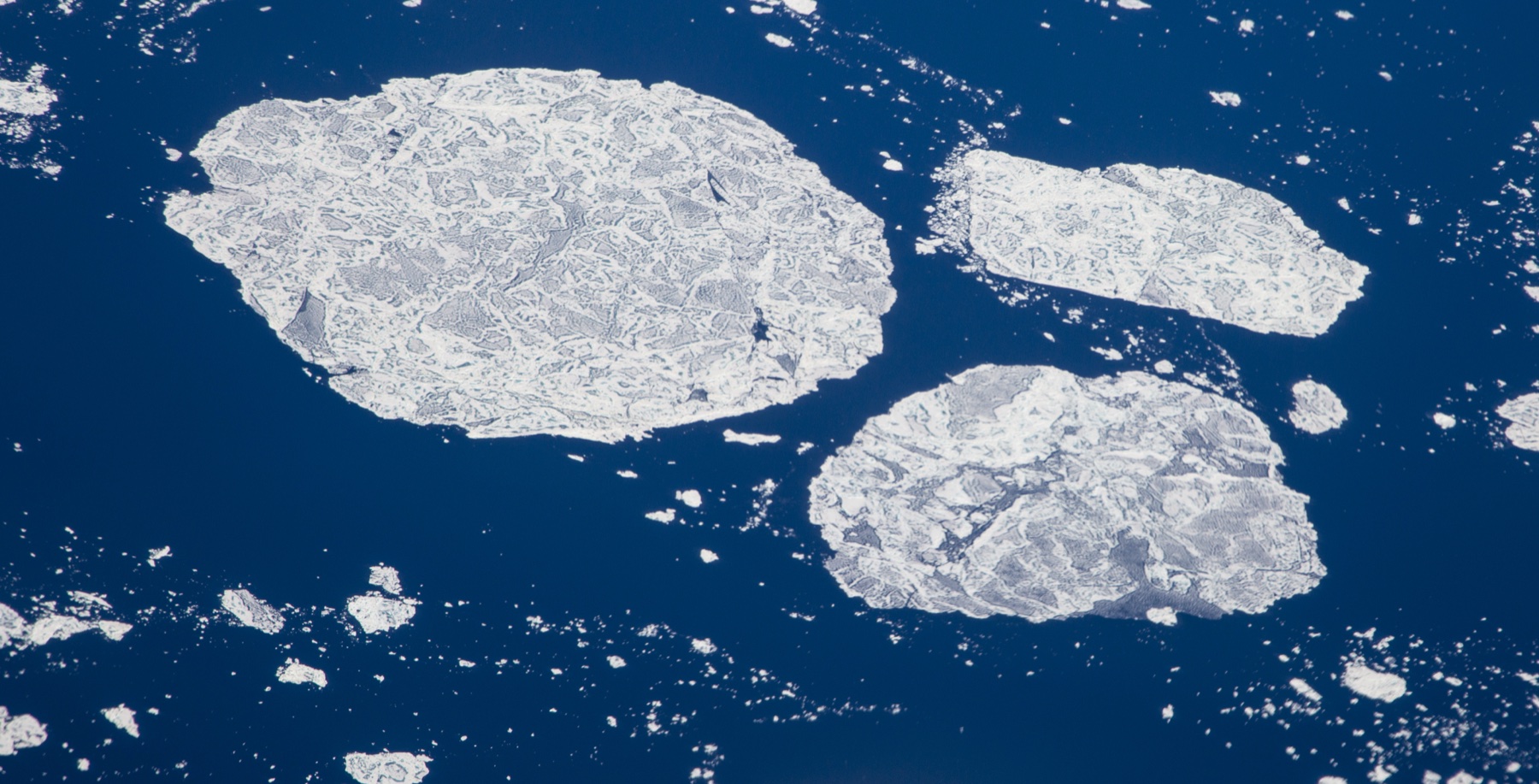 Aerial view of broken sea ice floes drifting on dark blue water in Hudson Strait